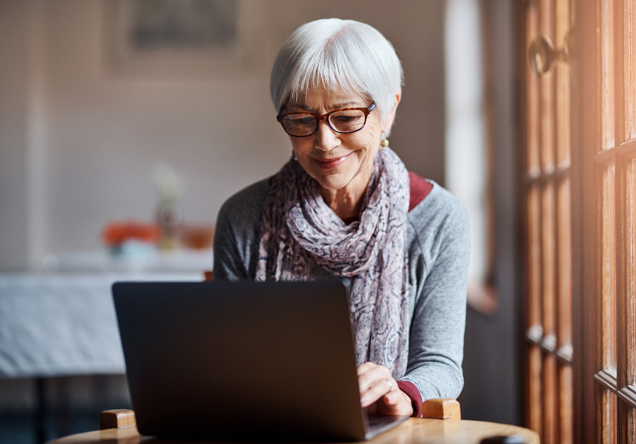 A smiling senior woman typing on a laptop.